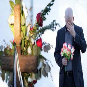 مردی ایستاده جلوی قبر با دسته گلی در دستش