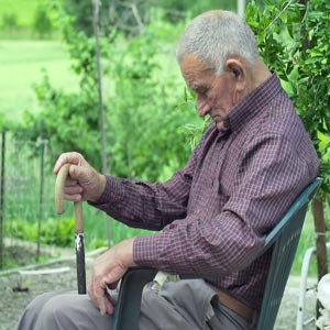 پیرمردی نشسته بر روی صندلی و عصا به دست در حال چرت زدن